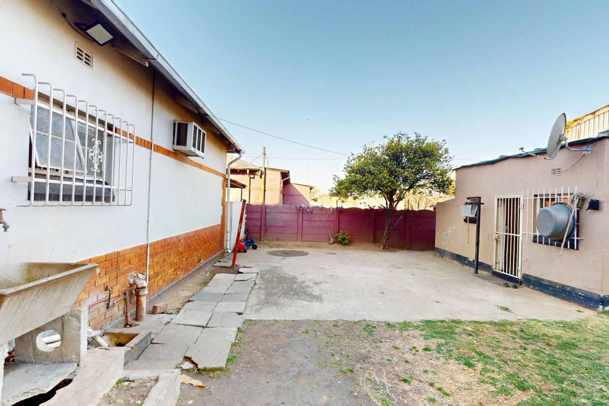 Rear exterior view of the property featuring a concrete paved yard, boundary wall, and external utility area with a fixed wash basin.