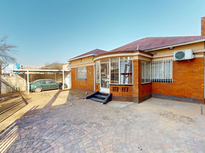 Front view of a brick house featuring a paved driveway, carport, security bars on windows, and an external air conditioning unit.