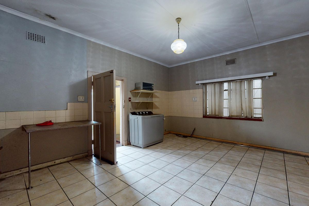 A dated kitchen area featuring tiled flooring, wall-mounted shelving, and a built-in sink, requiring cosmetic updates and repairs to the ceiling and walls.