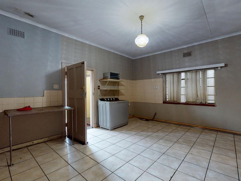 A dated kitchen area featuring tiled flooring, wall-mounted shelving, and a built-in sink, requiring cosmetic updates and repairs to the ceiling and walls.
