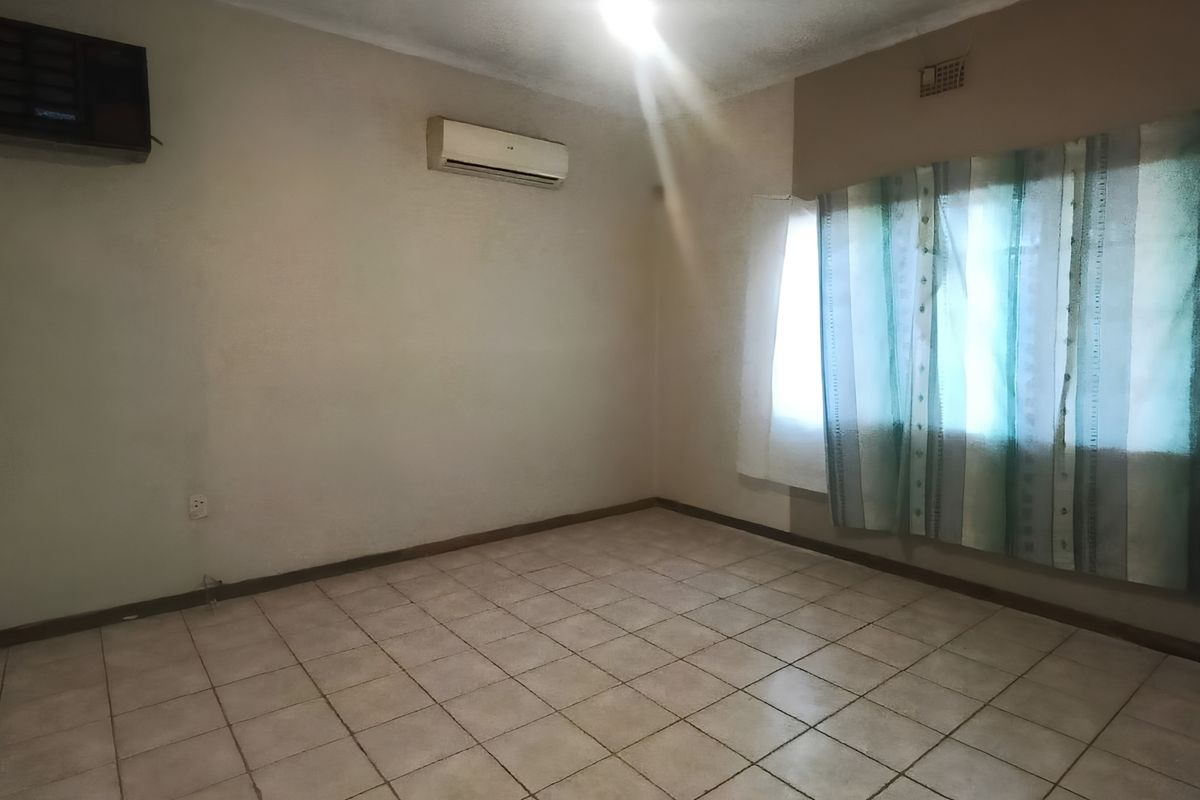 An empty living room featuring tiled flooring, a wall-mounted air conditioning unit, and a large window, providing a blank canvas for interior design.