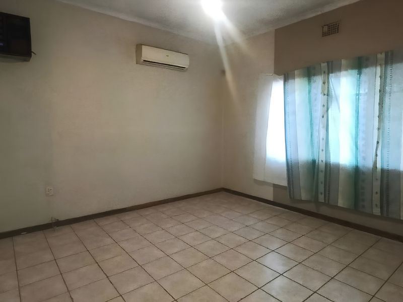 An empty living room featuring tiled flooring, a wall-mounted air conditioning unit, and a large window, providing a blank canvas for interior design.