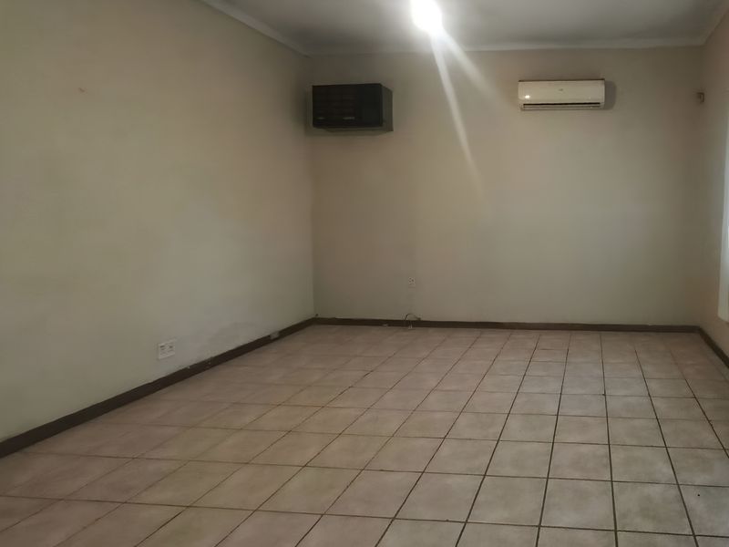 An empty living room featuring tiled flooring, a wall-mounted heater, and a split-system air conditioning unit.