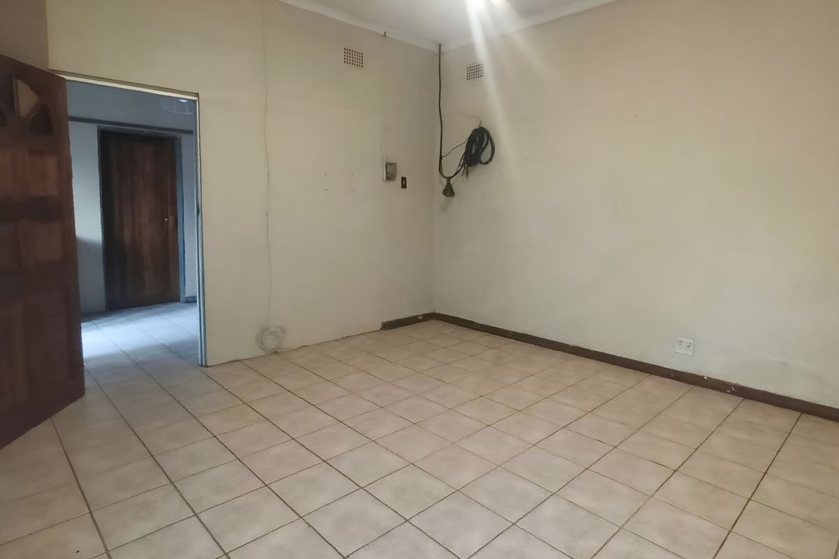 An empty bedroom featuring tiled flooring, a timber door, and basic electrical fixtures, requiring cosmetic updates to improve its overall condition.