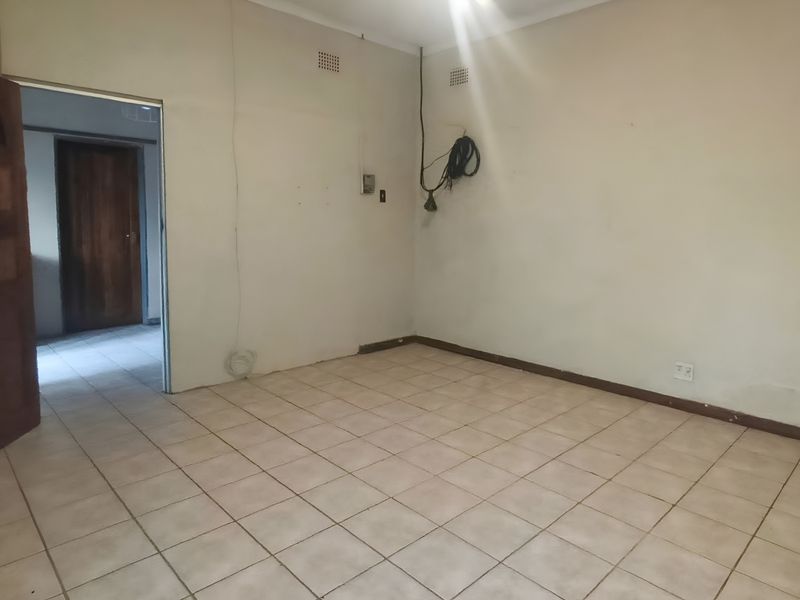 An empty bedroom featuring tiled flooring, a timber door, and basic electrical fixtures, requiring cosmetic updates to improve its overall condition.