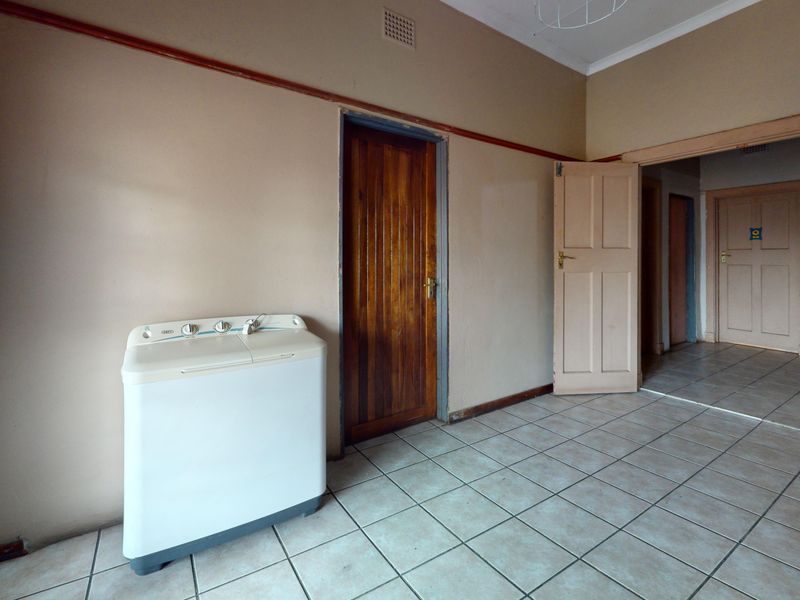 A functional laundry area featuring tiled flooring and multiple wooden doors, providing a blank canvas for renovation or utility space optimization.