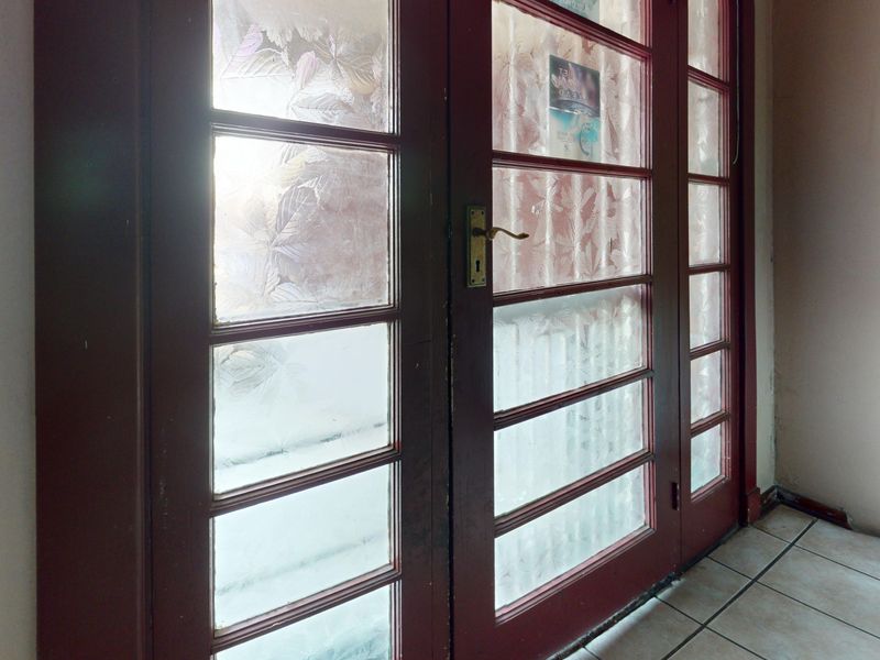 An entrance area featuring double glass panel doors with frosted detailing and tiled flooring, showing signs of wear on the door frames.