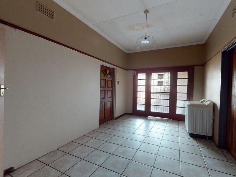 An empty entrance hall featuring tiled flooring, timber doors, and a glass-panelled door leading to the exterior.