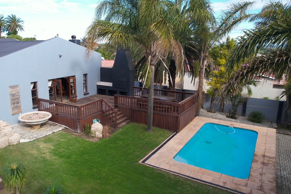 Aerial view of a rear garden featuring a swimming pool, raised timber deck with a built-in braai, and direct access to the house via french doors.