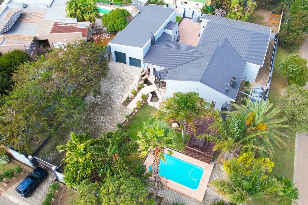 Aerial view of a residential property featuring a swimming pool, landscaped garden, water feature, paved driveway, and a double garage.