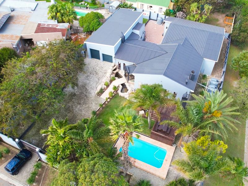 Aerial view of a residential property featuring a swimming pool, landscaped garden, water feature, paved driveway, and a double garage.
