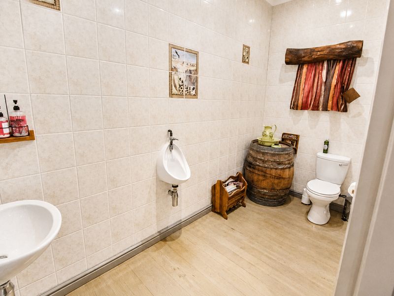 A functional bathroom featuring a wall-mounted urinal, standard toilet, and basin, finished with neutral ceramic wall tiles and wood-look laminate flooring.