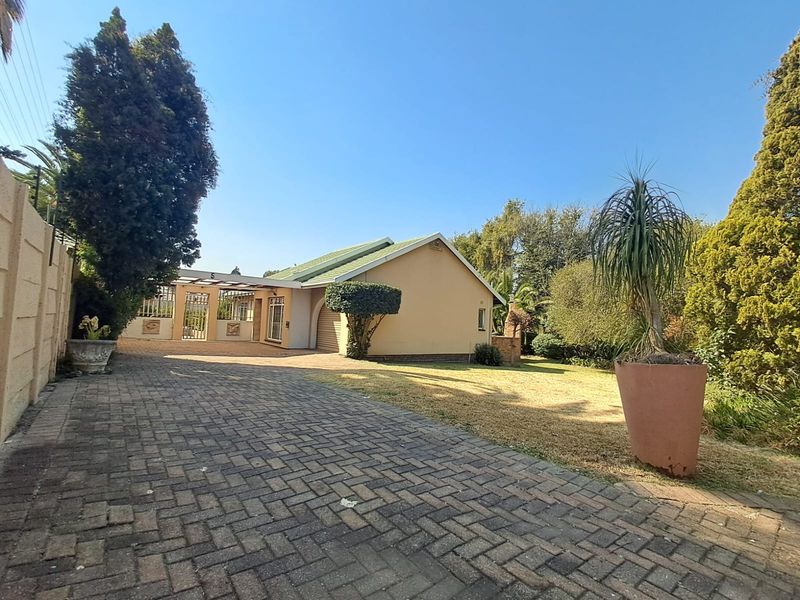Front view of the property featuring a paved driveway, carport, and established garden area with a brick boundary wall.