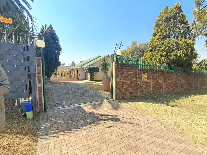 Front view of the property featuring a paved driveway, secure brick boundary wall with electric fencing, and access through a metal gate.