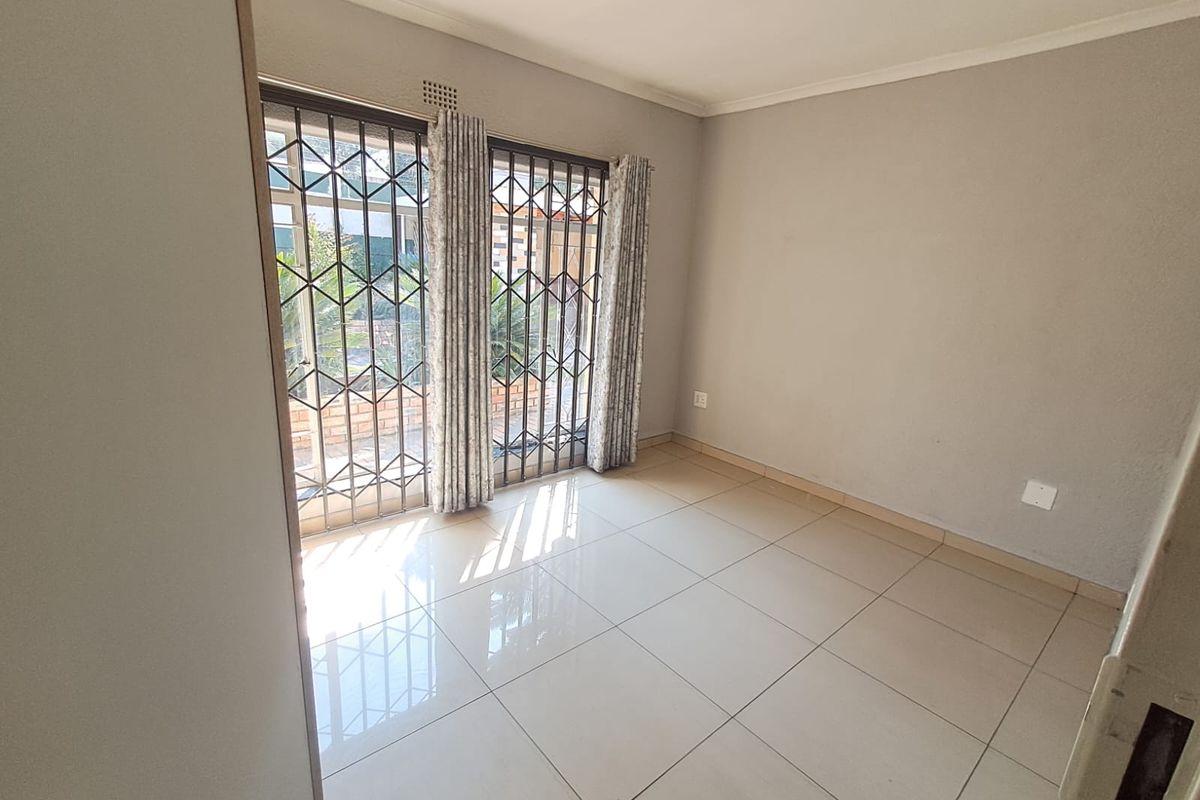 A bright, empty bedroom featuring neutral tiled flooring and sliding glass doors with integrated security gates, providing access to the exterior.