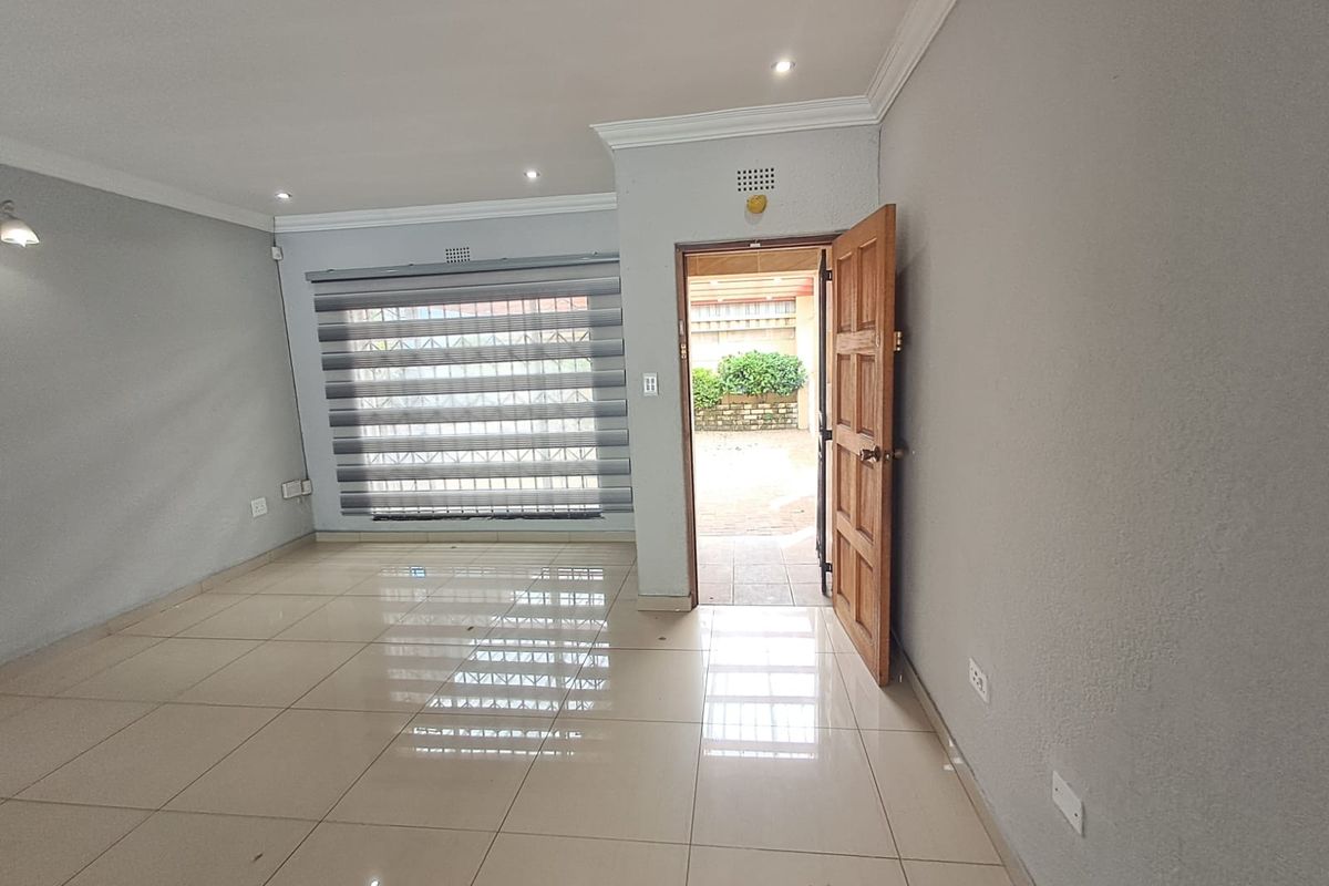 A bright, empty living room featuring neutral tiled flooring, recessed downlights, and modern zebra blinds, with direct access to an outdoor patio area.