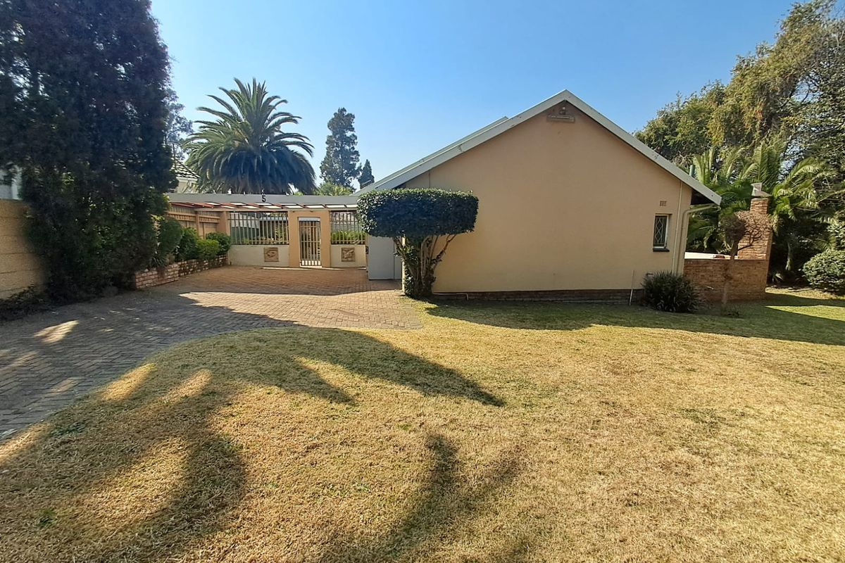 Rear view of the property featuring a paved driveway, covered patio area, and established garden with brick boundary walls.