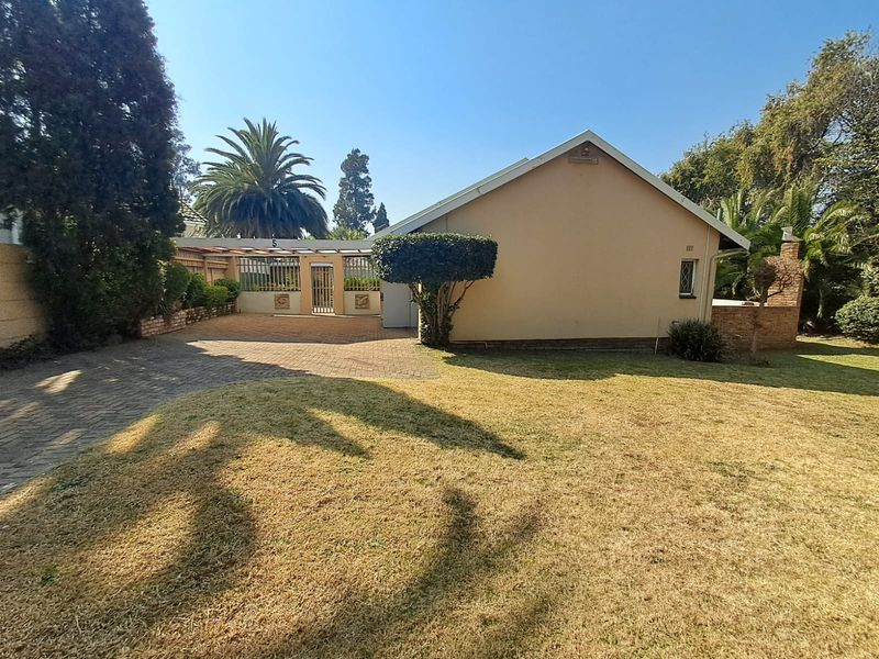 Rear view of the property featuring a paved driveway, covered patio area, and established garden with brick boundary walls.