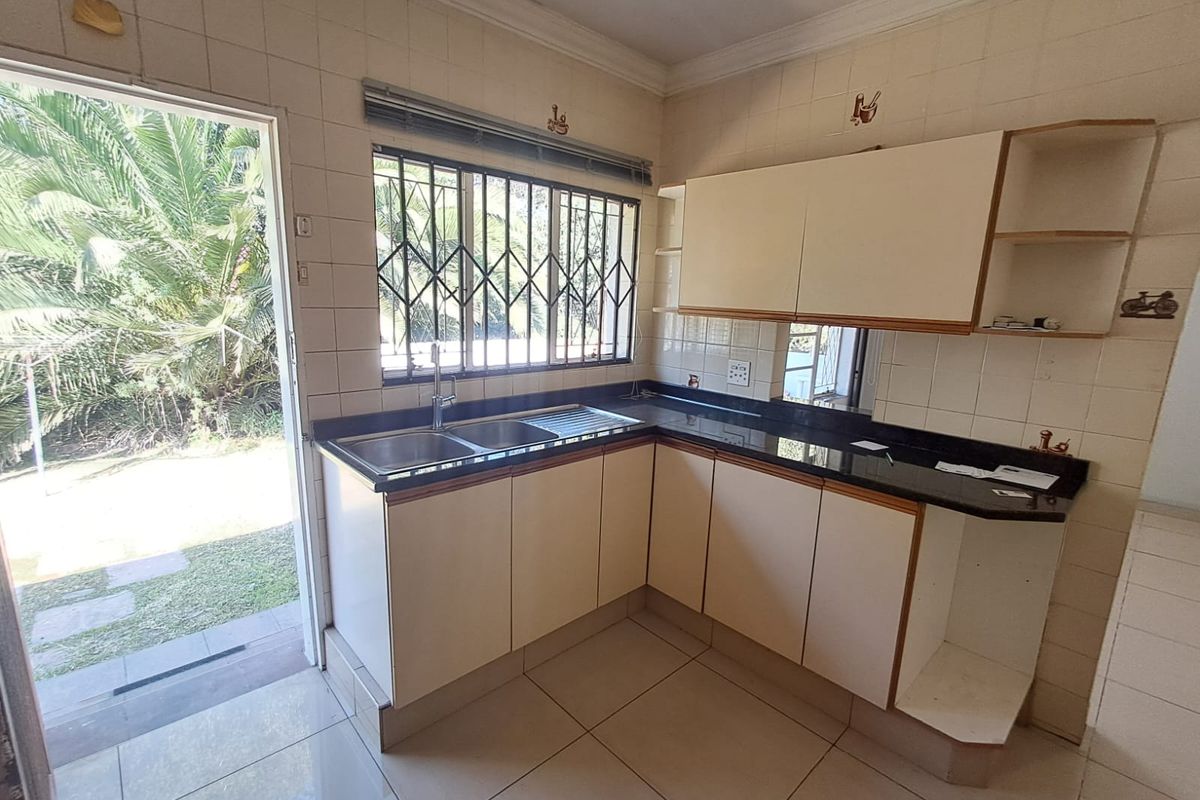 A functional kitchen featuring granite countertops, double sink, and built-in cabinetry with direct access to the garden area.