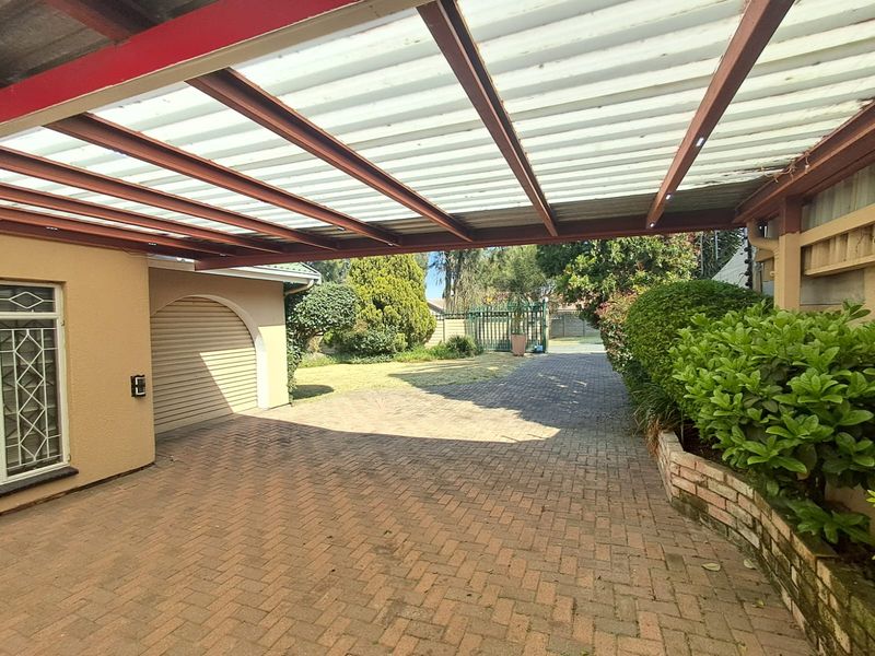 A covered carport area with a paved driveway, brick retaining wall, and secure gated access to the property.