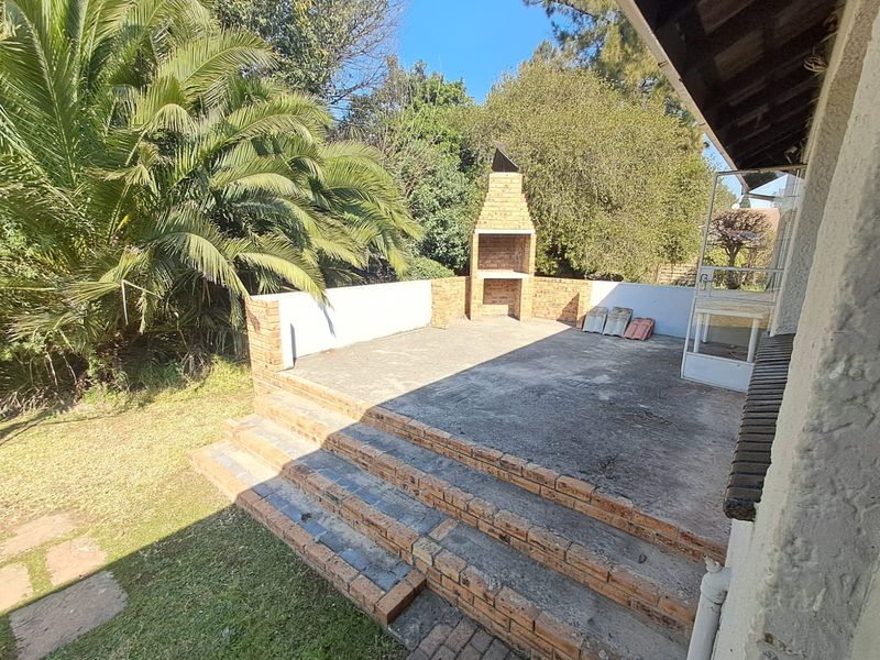 Outdoor patio area featuring a built-in brick braai, tiered brick steps, and a concrete floor, overlooking the garden.