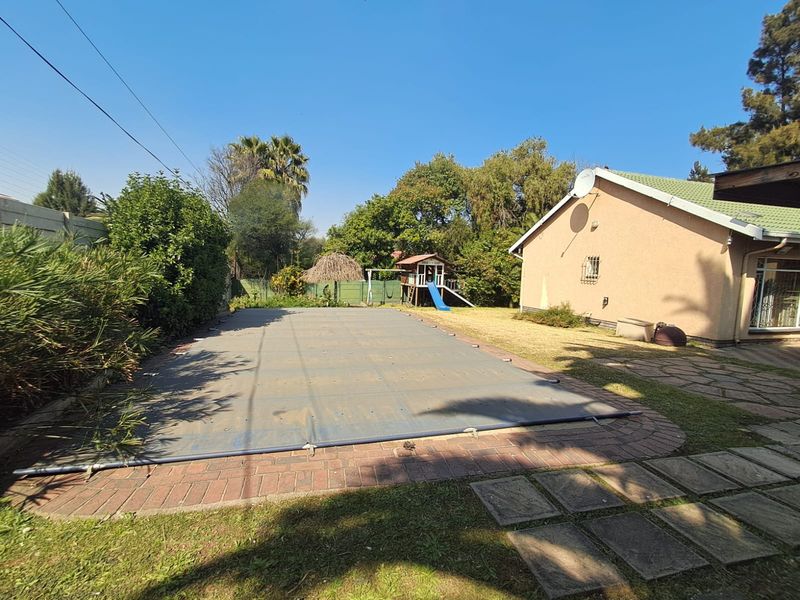 Rear garden area featuring a swimming pool with a safety cover, brick paved surround, and established lawn adjacent to the main house structure.