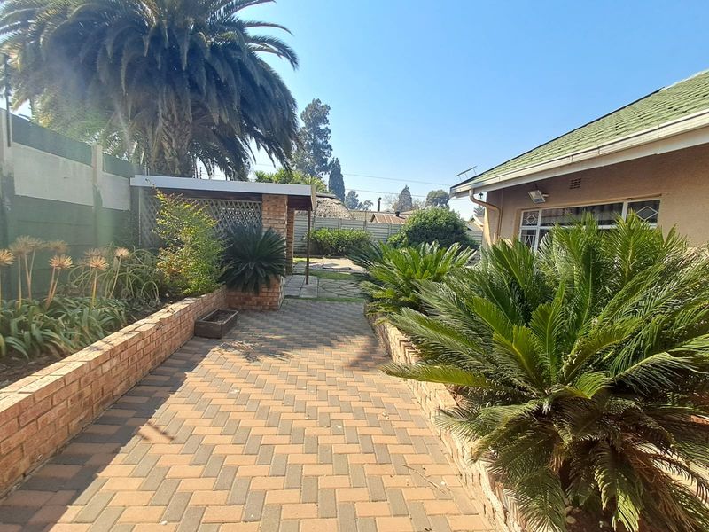 Rear garden area featuring brick paved pathways, established landscaping, brick retaining walls, and a covered patio section adjacent to the main house structure.