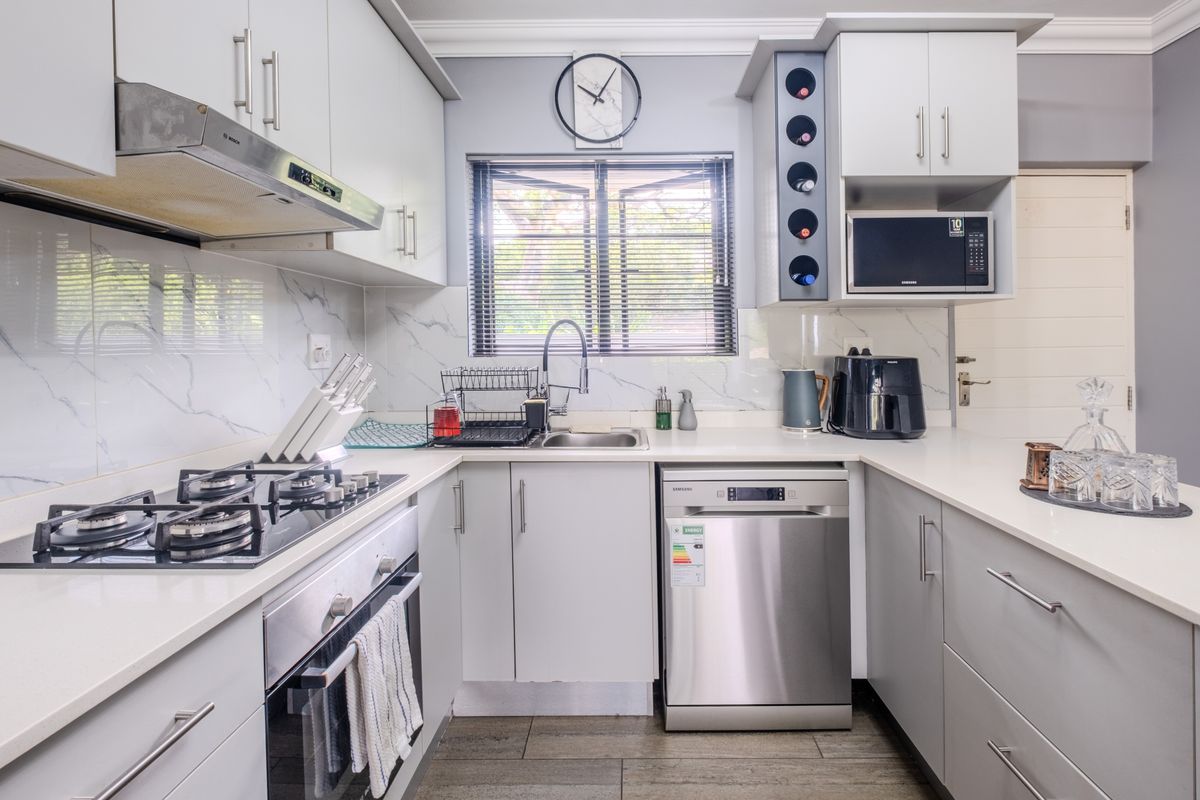 Modern kitchen featuring light grey cabinetry, quartz countertops, marble-look splashback, gas hob, built-in oven, and integrated dishwasher.