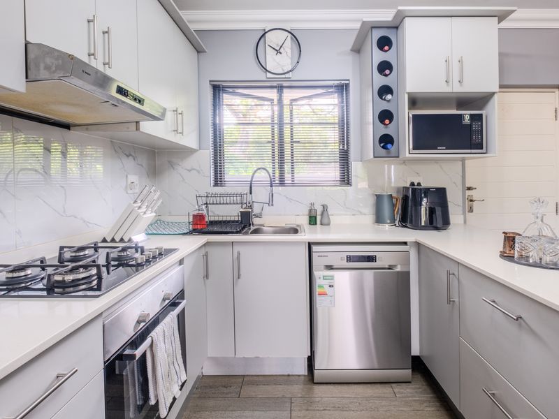 Modern kitchen featuring light grey cabinetry, quartz countertops, marble-look splashback, gas hob, built-in oven, and integrated dishwasher.