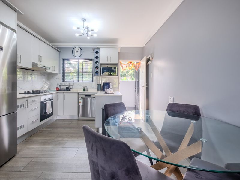 Modern open-plan kitchen and dining area featuring sleek white cabinetry, gas hob, integrated appliances, and contemporary tiled flooring.