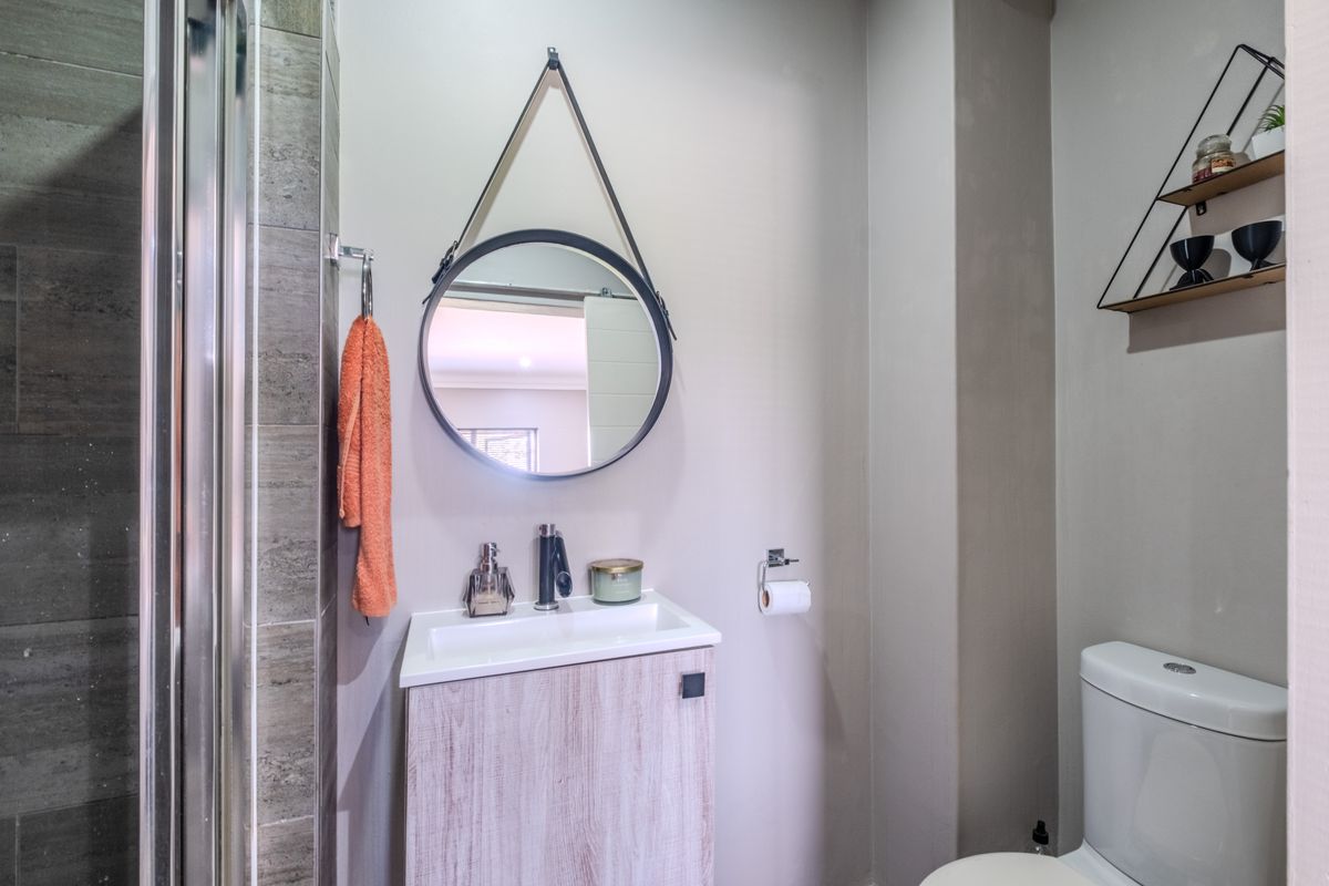 A modern bathroom featuring a vanity with basin, a toilet, and a glass-enclosed shower with tiled walls.