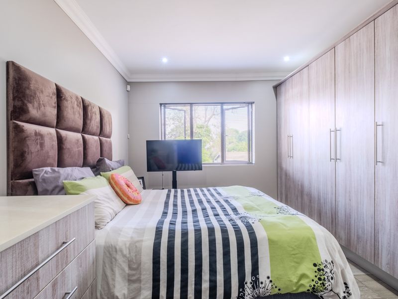 A well-maintained bedroom featuring extensive built-in cupboards, recessed downlighting, and neutral finishes, providing a clean and functional living space.