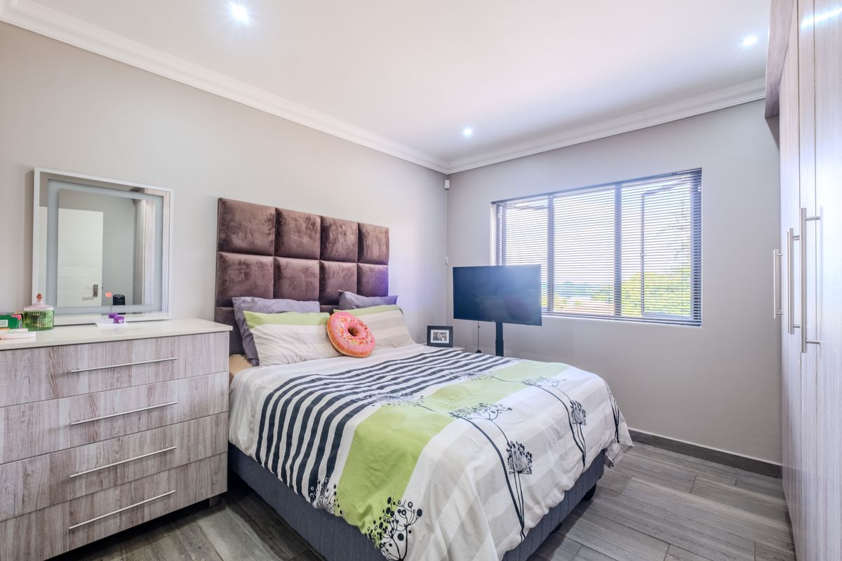 A well-maintained bedroom featuring built-in cupboards, tiled flooring, recessed downlighting, and large windows with venetian blinds.
