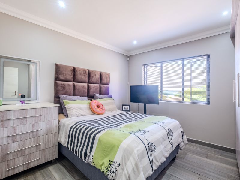 A well-maintained bedroom featuring built-in cupboards, tiled flooring, recessed downlighting, and large windows with venetian blinds.
