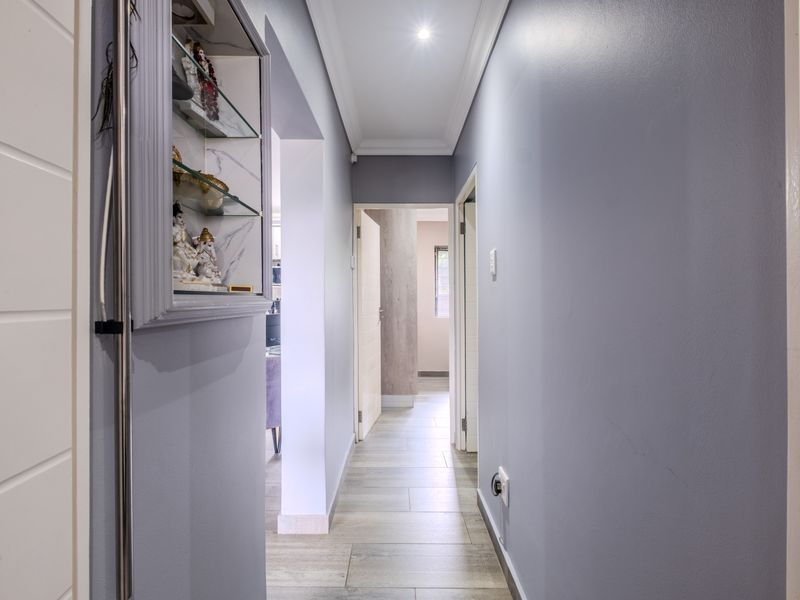 A well-lit hallway featuring tiled flooring, cove molding, and a built-in wall niche, providing access to multiple rooms within the apartment.