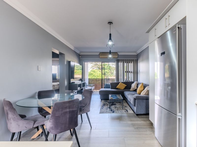 Open-plan living and dining area featuring tiled floors, modern pendant lighting, air conditioning, and direct access to a balcony through sliding glass doors.