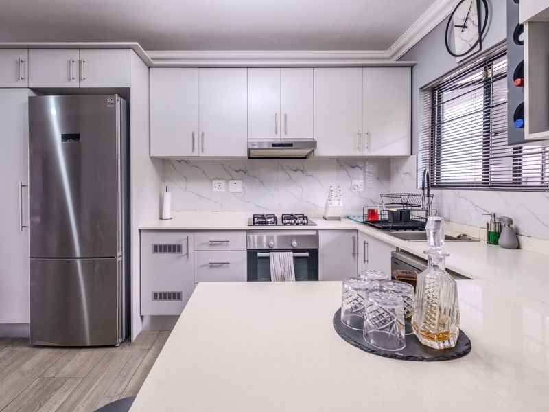 Modern kitchen featuring sleek white cabinetry, stone countertops, marble-look splashback, and integrated stainless steel appliances, offering a clean and functional cooking space.
