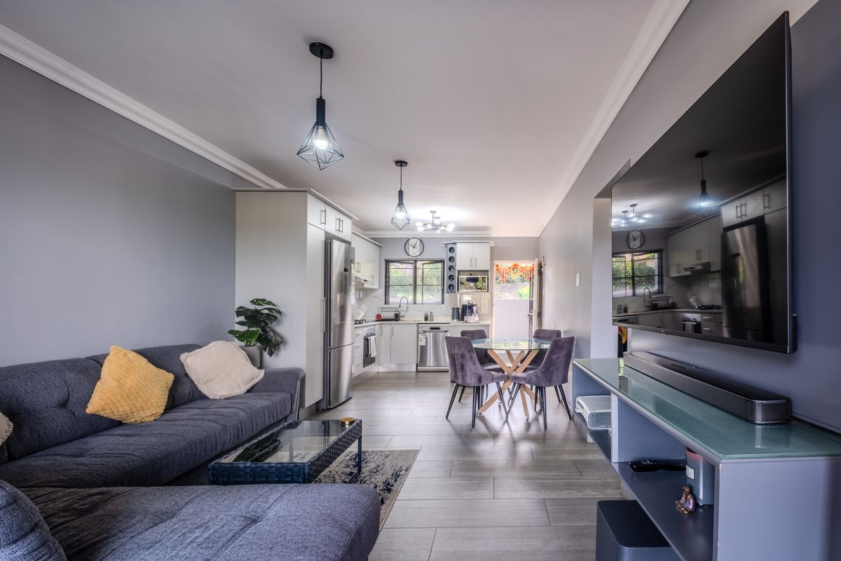 Modern open-plan living area featuring a well-appointed kitchen with built-in cabinetry, integrated appliances, and sleek tiled flooring throughout the combined space.