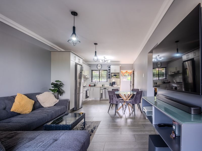 Modern open-plan living area featuring a well-appointed kitchen with built-in cabinetry, integrated appliances, and sleek tiled flooring throughout the combined space.