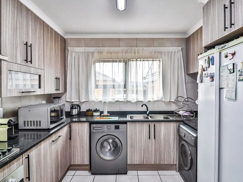 A functional kitchen featuring wood-look laminate cabinetry, granite countertops, a double basin sink, and integrated appliances including a hob and extractor fan.