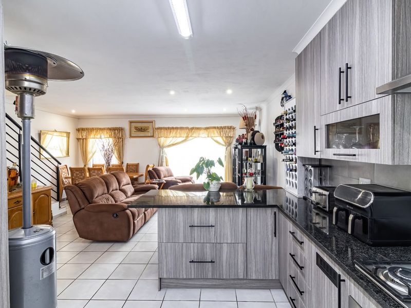 Open-plan living area featuring a modern kitchen with granite countertops, gas hob, and integrated cabinetry, flowing into a spacious lounge with staircase access.