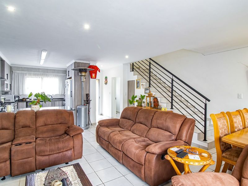 Open-plan living and kitchen area featuring tiled floors, a staircase with metal balustrades, and functional kitchen cabinetry.