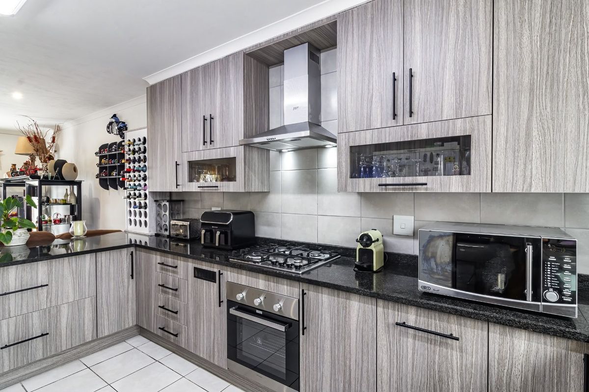 Modern kitchen featuring wood-grain cabinetry, granite countertops, a gas hob, built-in oven, and stainless steel extractor fan with a tiled backsplash.