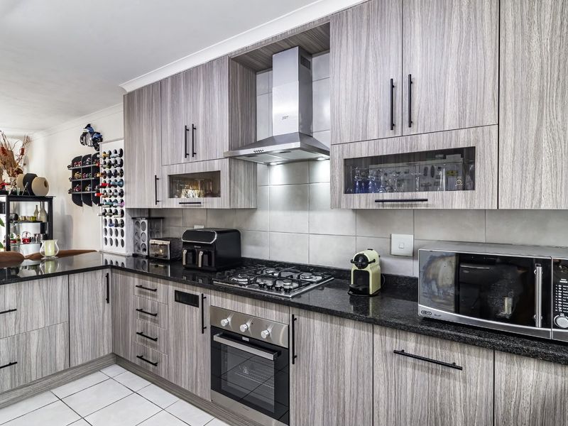 Modern kitchen featuring wood-grain cabinetry, granite countertops, a gas hob, built-in oven, and stainless steel extractor fan with a tiled backsplash.