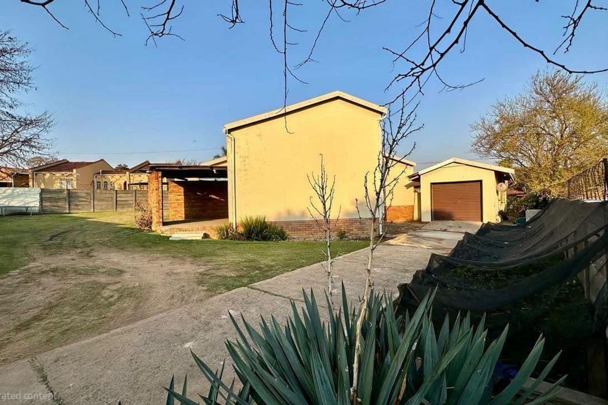Rear view of the property featuring a concrete driveway, covered patio area, detached garage, and a spacious garden with perimeter walling.