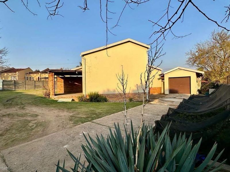 Rear view of the property featuring a concrete driveway, covered patio area, detached garage, and a spacious garden with perimeter walling.