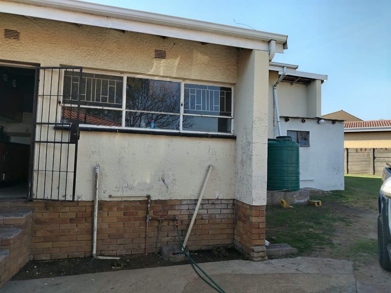 Rear exterior view of the house featuring a water tank, security bars on windows, and exposed brick and plaster finishes.