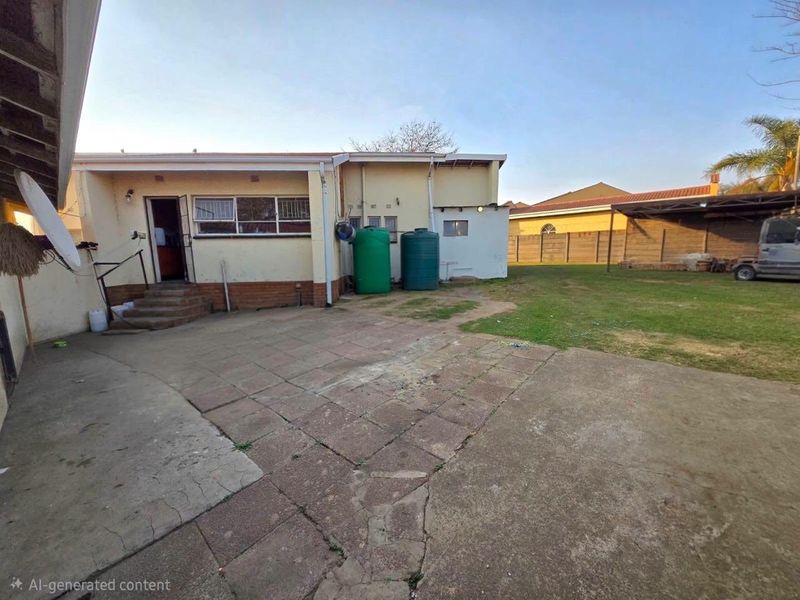 Rear exterior view featuring a paved patio area, water storage tanks, and a spacious backyard with a brick boundary wall.