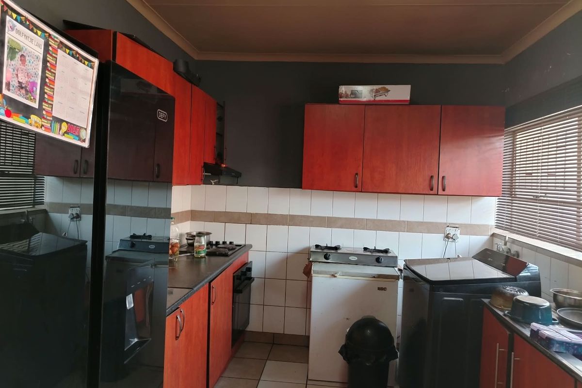 A functional kitchen featuring wooden cabinetry, tiled backsplash, gas hob, and oven, with neutral tiled flooring and window blinds.