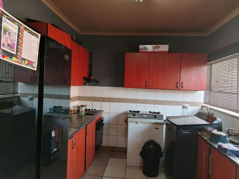 A functional kitchen featuring wooden cabinetry, tiled backsplash, gas hob, and oven, with neutral tiled flooring and window blinds.